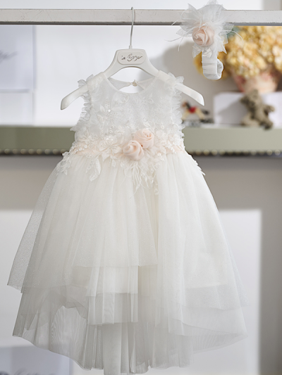 Η διαχρονική κομψότητα και η εκλεπτυσμένη αισθητική χαρακτηρίζουν αυτό το εντυπωσιακό βαπτιστικό φόρεμα σε off white απόχρωση. Το κορσάζ είναι διακοσμημένο με εκλεπτυσμένη δαντέλα και ανάγλυφα απλικέ μοτίβα, που χαρίζουν πλούσια υφή και ιδιαίτερο χαρακτήρα. Στη μέση, μια σατέν ζώνη σε απαλό σομόν τόνο στολίζεται με χειροποίητα λουλούδια και διακριτικές λεπτομέρειες από τούλι, προσθέτοντας μια κομψή χρωματική πινελιά.