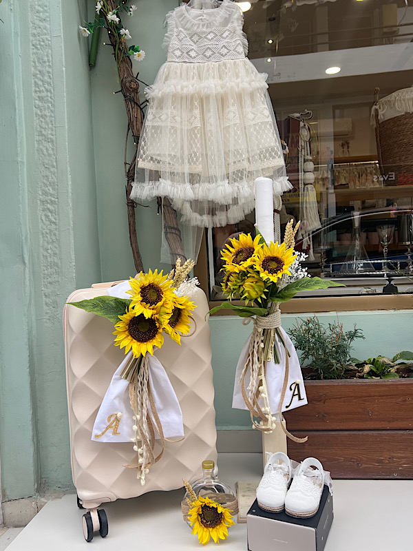 Βαπτιστικό πακέτο boho με ηλιοτρόπια και βαλίτσα Ένα ολοκληρωμένο ξεχωριστό βαπτιστικό πακέτο σε λευκές και φυσικές αποχρώσεις , με πρωταγωνιστές τα εντυπωσιακά ηλιοτρόπια που χαρίζουν ζεστασιά , φρεσκάδα και καλοκαιρινή διάθεση ! Το σετ συνδυάζει κομψές λεπτομέρειες , φυσικά στοιχεία και διακριτικές χρυσές πινελιές , δημιουργώντας μια ατονική σύνθεση που ξεχωρίζει για την αισθητική και τη μοναδικότητα της. Το boho βαπτιστικό φόρεμα από εκρού τούλι με εντυπωσιακές δαντελένιες λεπτομέρειες ολοκληρώνει υπέροχα το σύνολο μαζί με τις ασορτί εσπαντρίγιες.